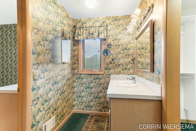 bathroom with wallpapered walls, baseboards, visible vents, and vanity