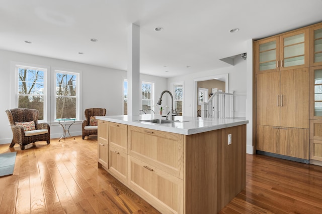 kitchen with a center island with sink, light countertops, light brown cabinets, a sink, and hardwood / wood-style floors