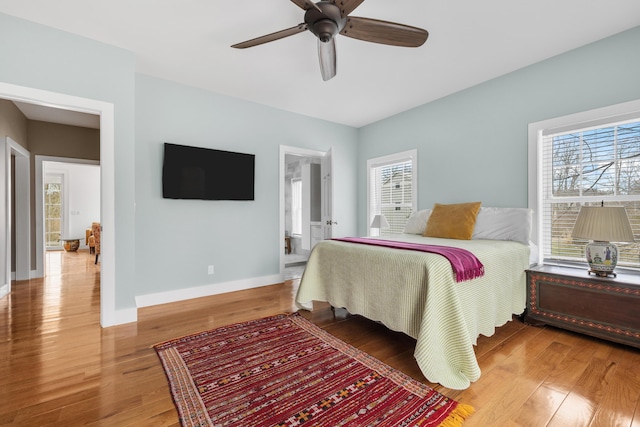 bedroom featuring a ceiling fan, ensuite bath, baseboards, and wood finished floors