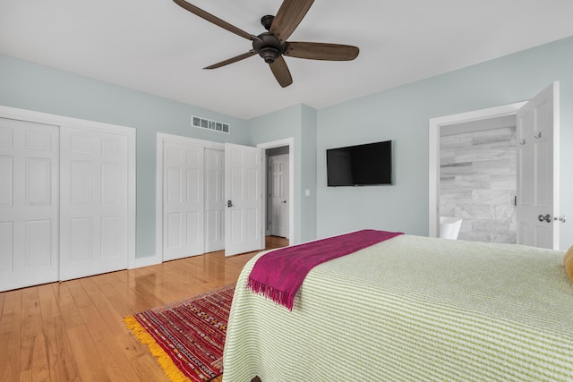 bedroom with wood finished floors, visible vents, ceiling fan, and two closets