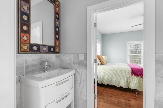 ensuite bathroom with ensuite bath, tile walls, vanity, and wood finished floors