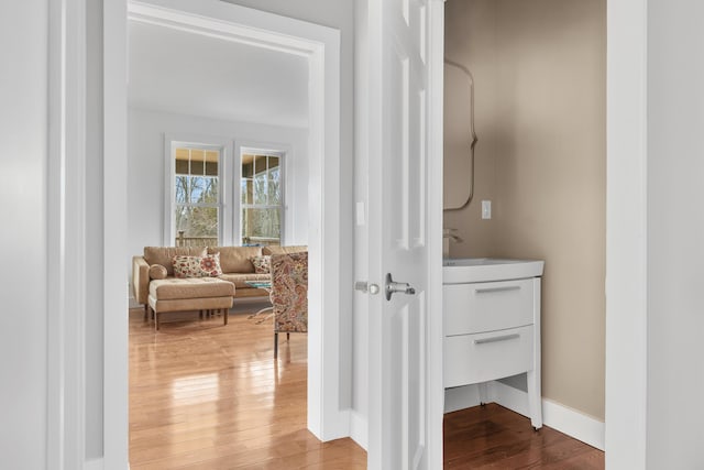 hall featuring a sink, baseboards, and wood finished floors