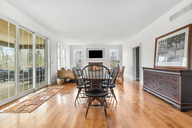 dining space with light wood-style floors, visible vents, a fireplace, and baseboards