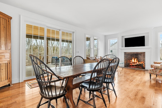 dining space with a tiled fireplace and light wood-style flooring