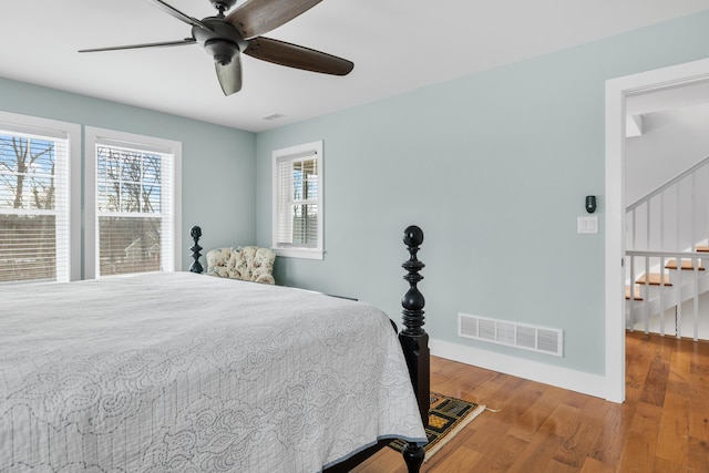 bedroom with a ceiling fan, wood finished floors, visible vents, and baseboards