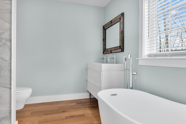 full bathroom featuring toilet, wood finished floors, vanity, baseboards, and a freestanding bath