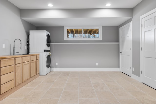 laundry area featuring stacked washer and clothes dryer, cabinet space, a sink, and baseboards