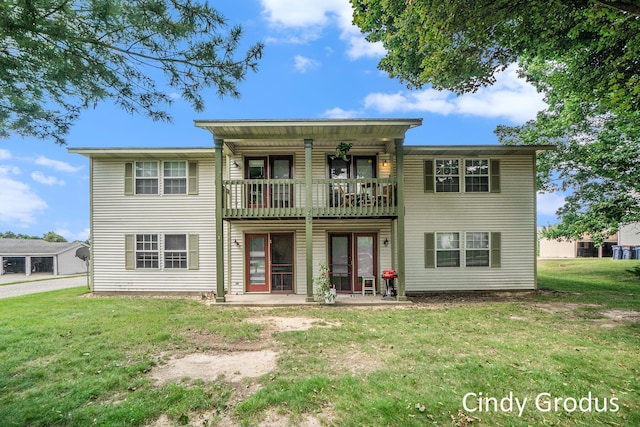 rear view of property featuring a lawn, a balcony, and a patio