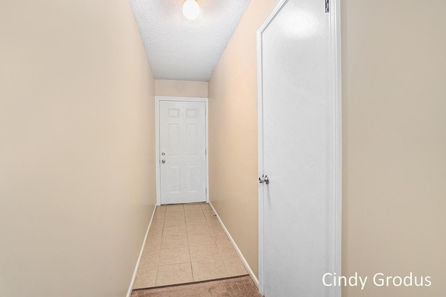 corridor featuring light tile patterned floors, baseboards, and a textured ceiling