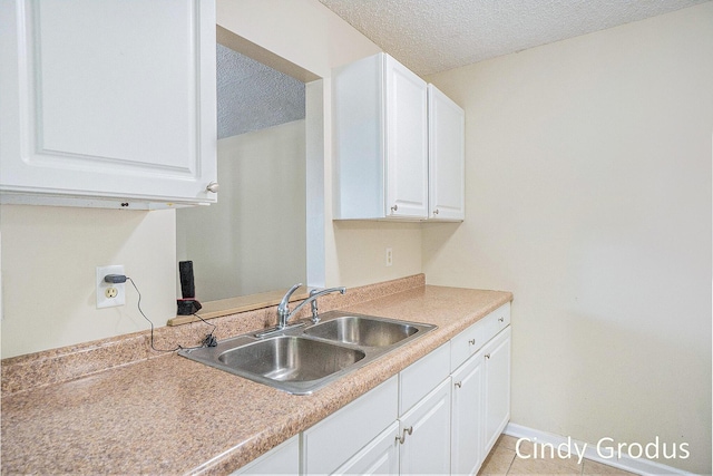 kitchen featuring baseboards, light countertops, a textured ceiling, white cabinetry, and a sink