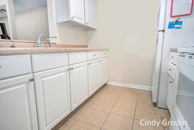 kitchen with light tile patterned floors, white cabinetry, light countertops, and freestanding refrigerator