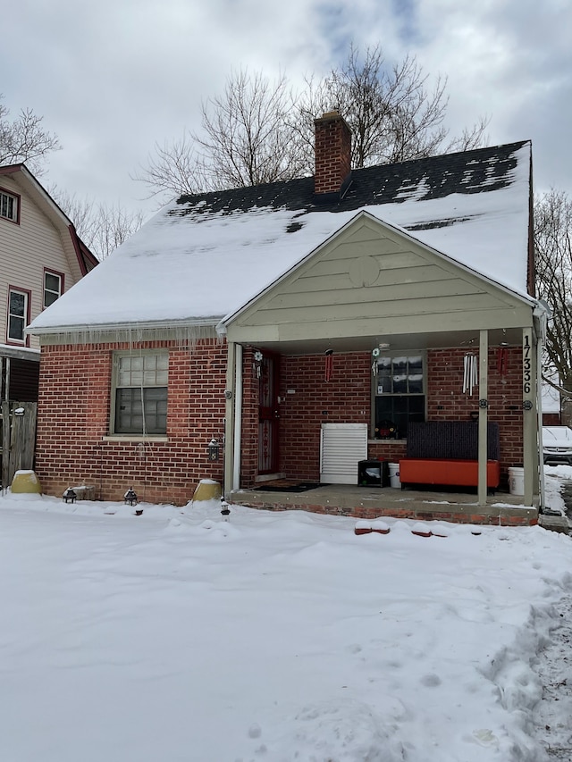 view of front of property with covered porch, brick siding, and a chimney