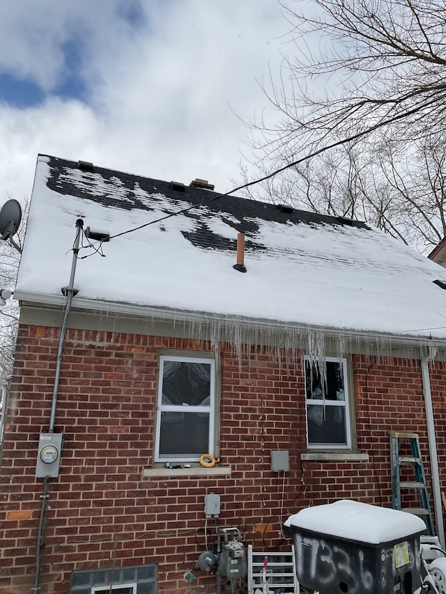 snow covered property with brick siding and cooling unit