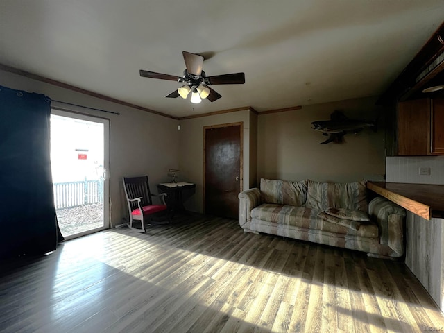 living area with ornamental molding, wood finished floors, and a ceiling fan