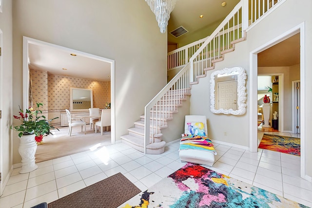 staircase with wallpapered walls, visible vents, baseboards, a towering ceiling, and tile patterned flooring