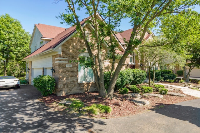 view of side of property with brick siding, an attached garage, and aphalt driveway