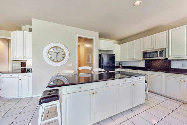 kitchen with a center island, light tile patterned floors, stainless steel microwave, freestanding refrigerator, and white cabinetry