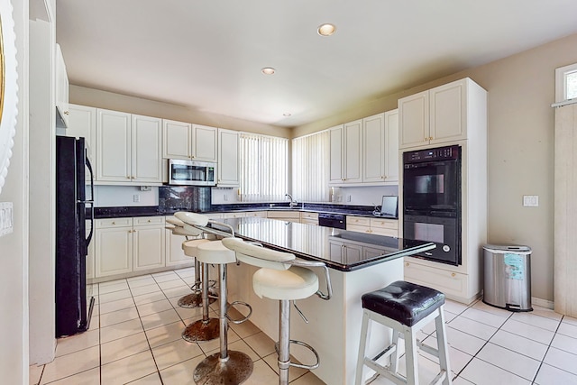 kitchen with light tile patterned floors, black appliances, a breakfast bar area, and a kitchen island