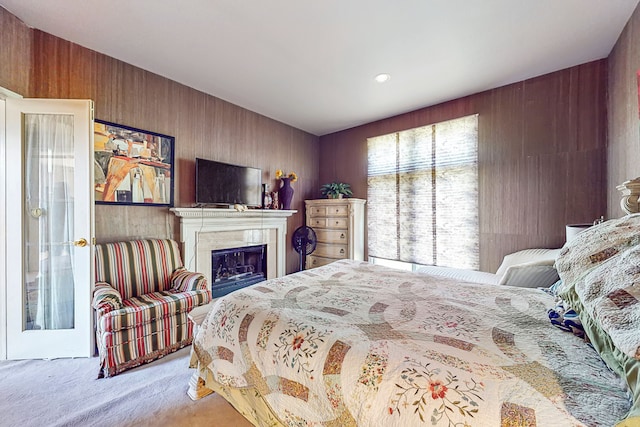 bedroom featuring carpet floors, wood walls, and a glass covered fireplace