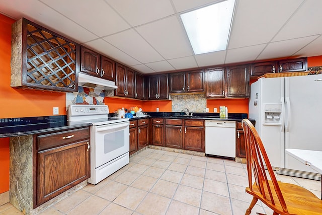 kitchen featuring dark countertops, white appliances, under cabinet range hood, and light tile patterned floors