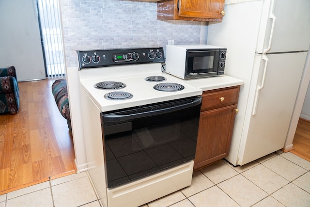 kitchen with black microwave, electric stove, light countertops, freestanding refrigerator, and brown cabinets