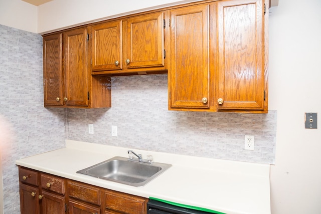 kitchen with light countertops, backsplash, brown cabinetry, a sink, and dishwashing machine