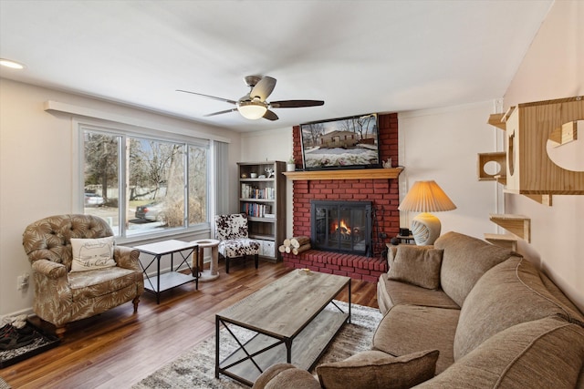 living area featuring a ceiling fan, a fireplace, and wood finished floors