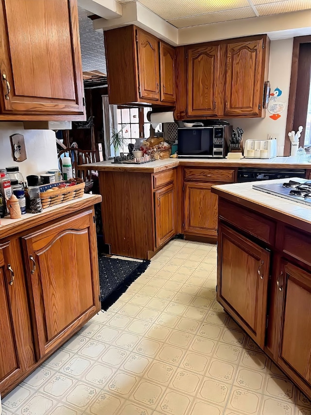 kitchen with brown cabinetry, a peninsula, light countertops, light floors, and black microwave