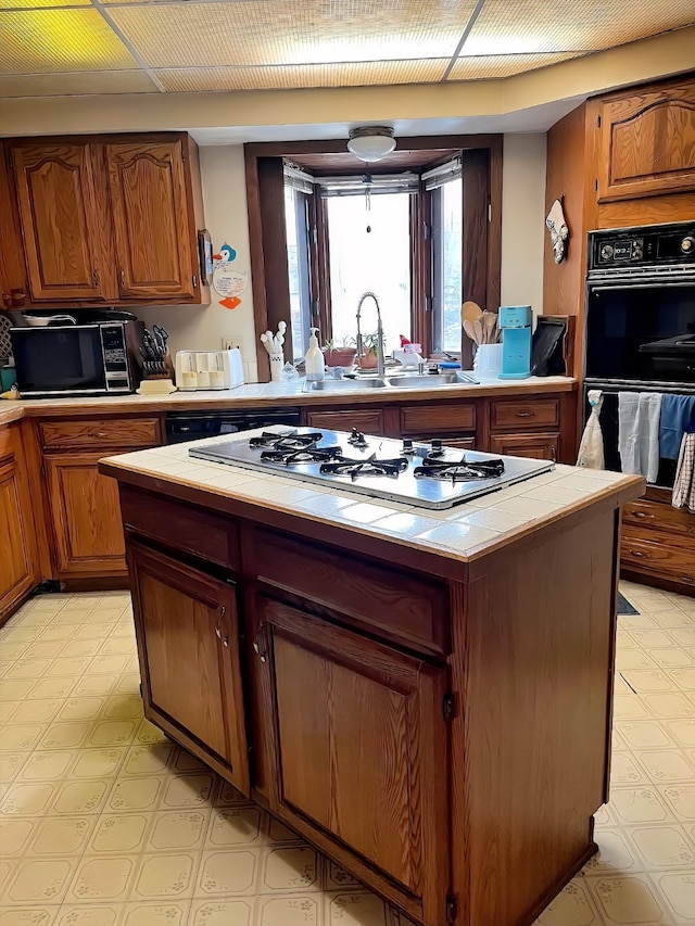 kitchen with tile countertops, black appliances, brown cabinets, and a center island