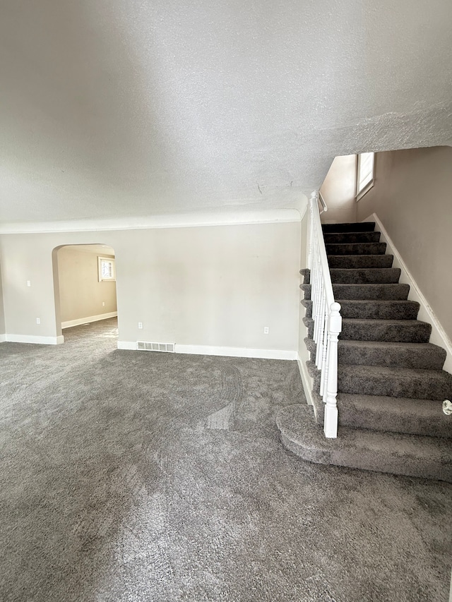 interior space featuring arched walkways, visible vents, a textured ceiling, baseboards, and stairs