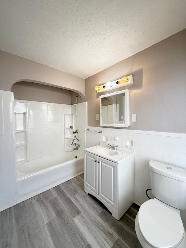 bathroom with a textured ceiling, toilet, wood finished floors, tile walls, and washtub / shower combination