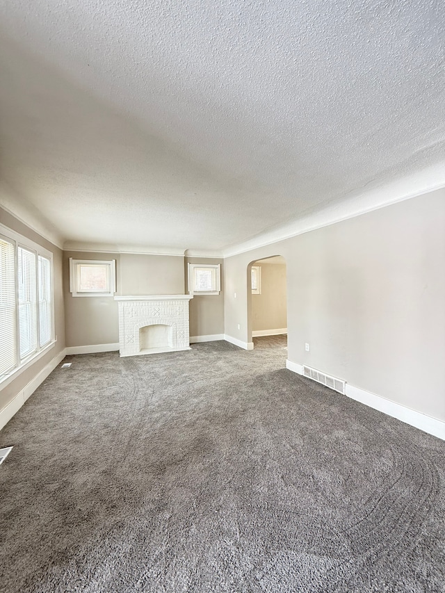 unfurnished living room with visible vents, arched walkways, a healthy amount of sunlight, carpet floors, and a fireplace