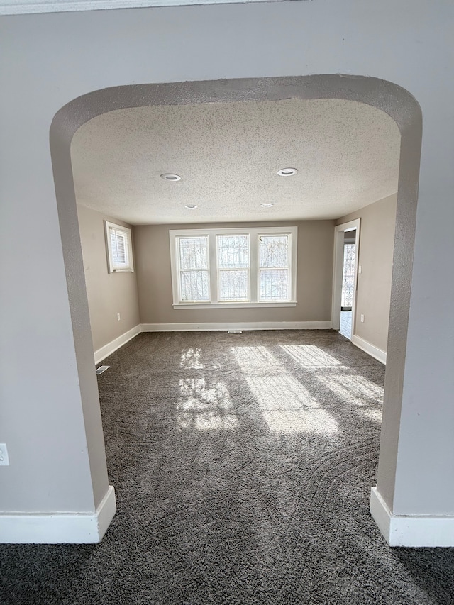 unfurnished room featuring baseboards, carpet, arched walkways, and a textured ceiling