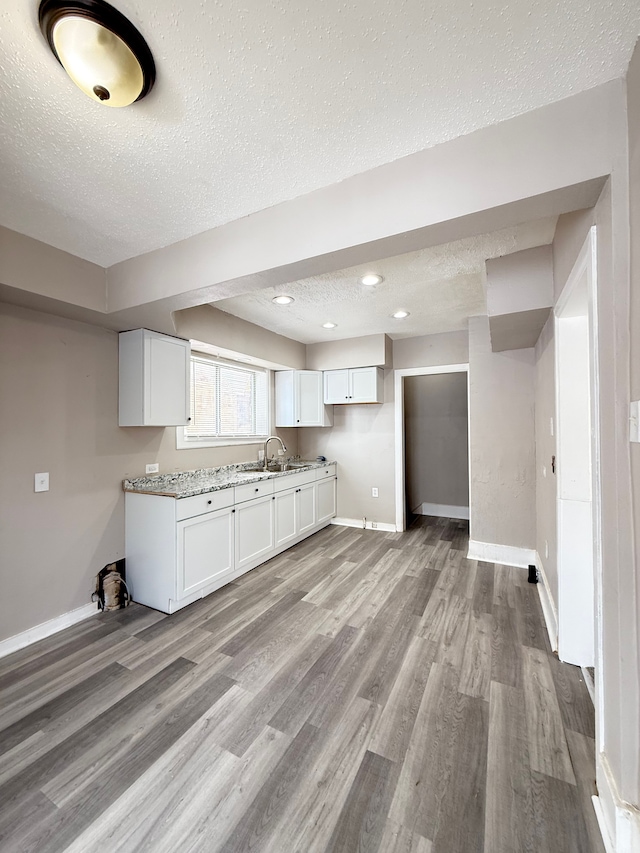 kitchen featuring a textured ceiling, a sink, white cabinetry, and light wood-style floors