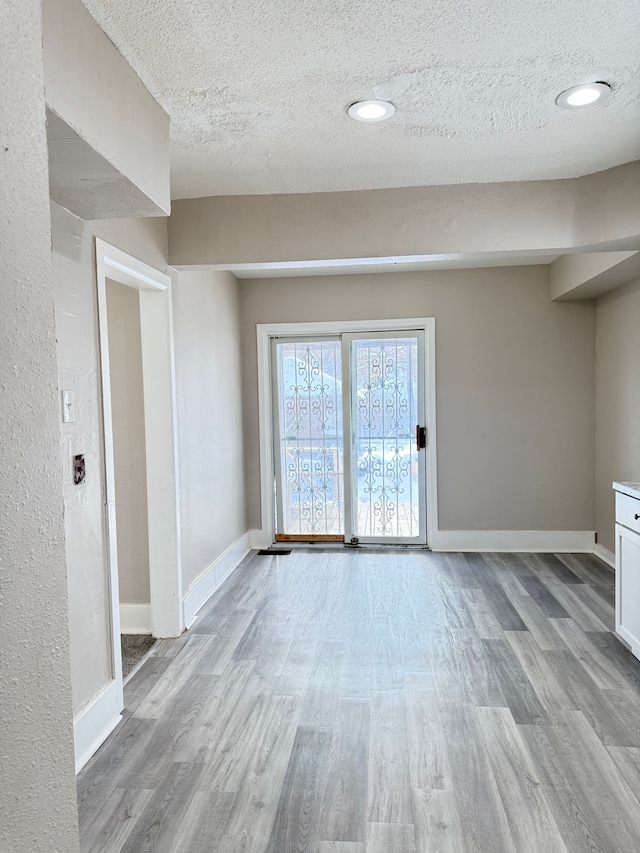 empty room featuring a textured ceiling, recessed lighting, wood finished floors, and baseboards