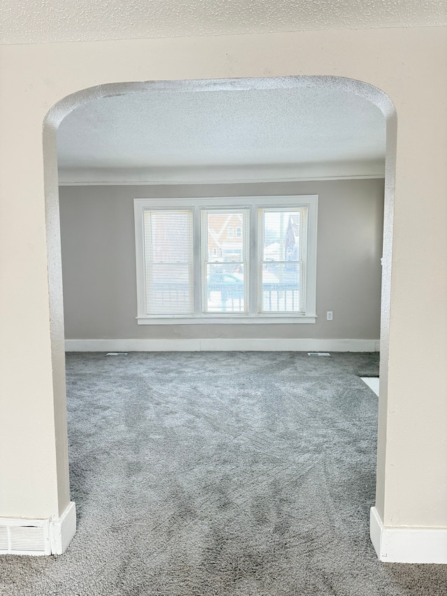 carpeted spare room with arched walkways, a textured ceiling, and baseboards