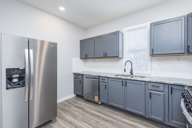 kitchen with light wood-style flooring, appliances with stainless steel finishes, tasteful backsplash, and a sink