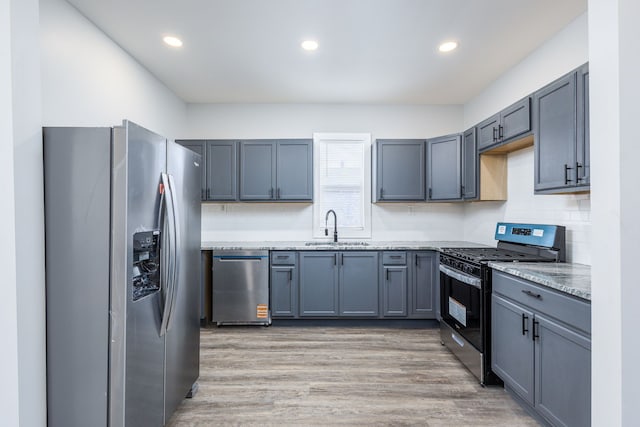 kitchen with a sink, appliances with stainless steel finishes, light wood-type flooring, decorative backsplash, and light stone countertops