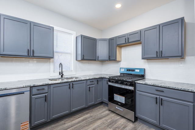 kitchen with light stone counters, decorative backsplash, appliances with stainless steel finishes, a sink, and wood finished floors