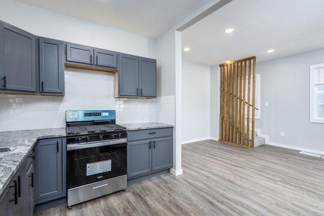 kitchen with light stone countertops, stainless steel gas range, tasteful backsplash, and light wood-style floors