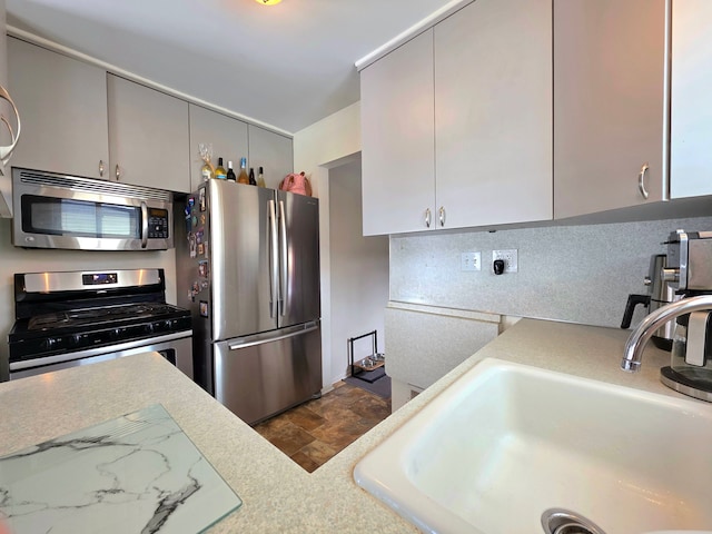 kitchen with light countertops, gray cabinetry, appliances with stainless steel finishes, stone finish floor, and a sink