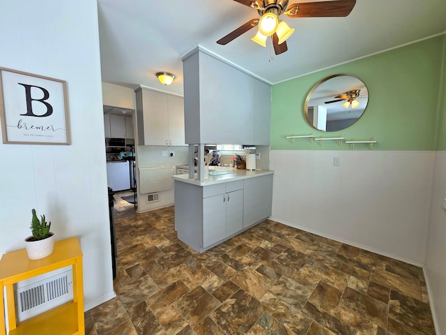 kitchen with a wainscoted wall, light countertops, visible vents, stone finish floor, and a peninsula