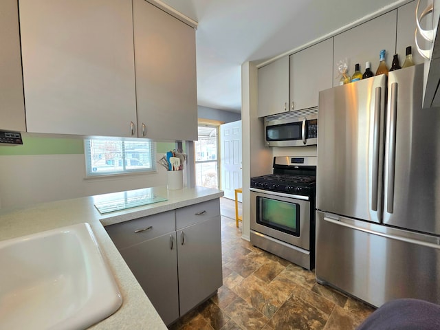 kitchen with appliances with stainless steel finishes, light countertops, a sink, and gray cabinetry