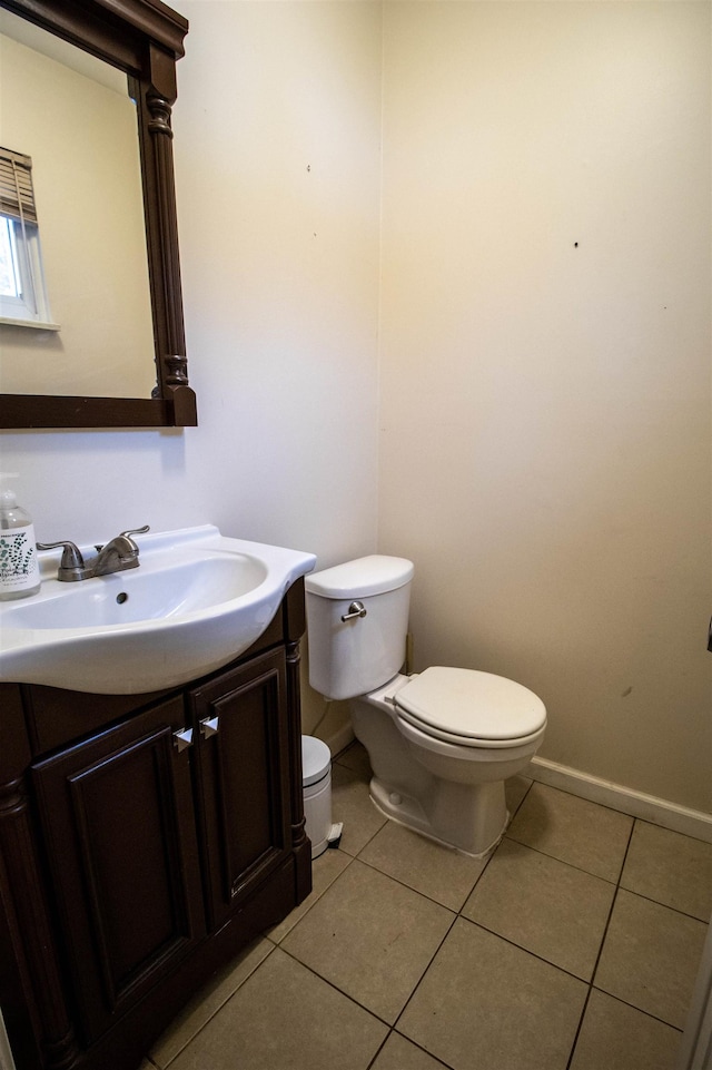 half bathroom with toilet, vanity, tile patterned floors, and baseboards