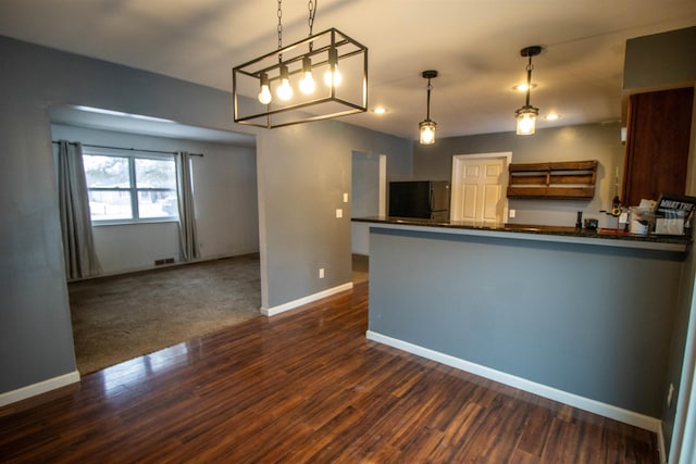 kitchen with a peninsula, dark wood-style flooring, baseboards, freestanding refrigerator, and dark countertops