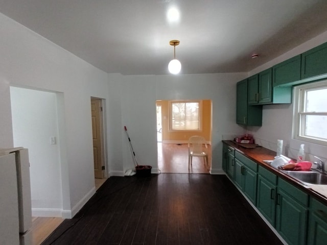 kitchen with green cabinets, a sink, dark wood finished floors, and baseboards