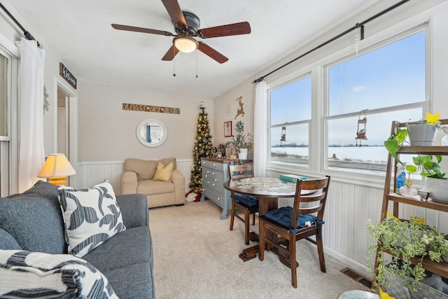 living area featuring a ceiling fan, light colored carpet, a wainscoted wall, and visible vents