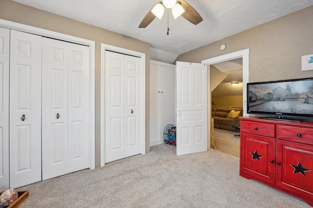 bedroom featuring carpet floors, multiple closets, lofted ceiling, a ceiling fan, and a textured ceiling