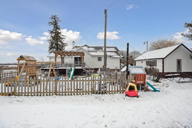 snow covered back of property featuring a playground, fence, and a pergola