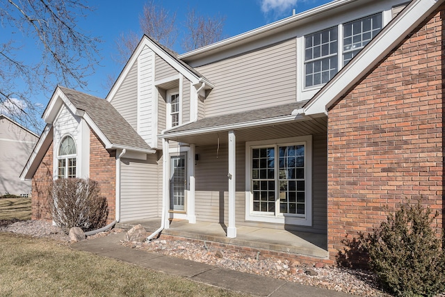 view of front of house featuring covered porch, a shingled roof, and brick siding